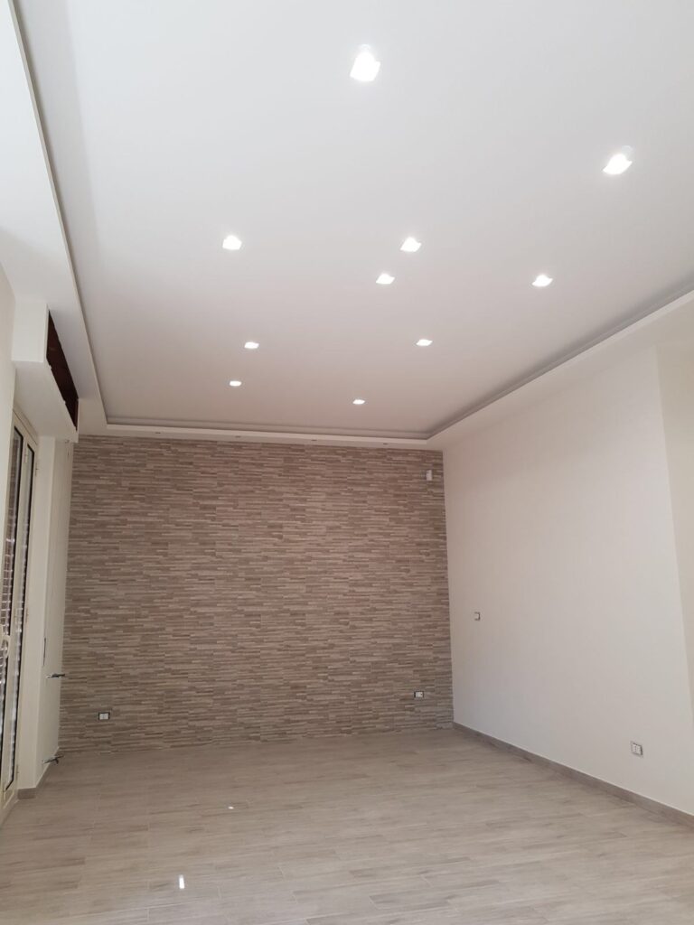 Controsoffitto con faretti incassati in un ambiente con parete rivestita effetto pietra